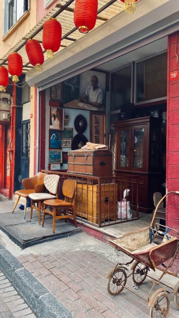 Explore a charming antique shop with vintage decor, chairs, trunks, and red lanterns.