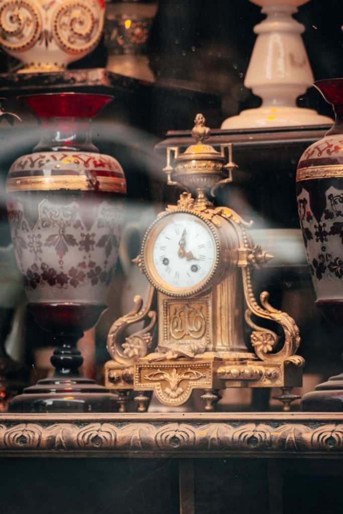 An ornate gold clock surrounded by vintage vases in an elegant shop window display.
